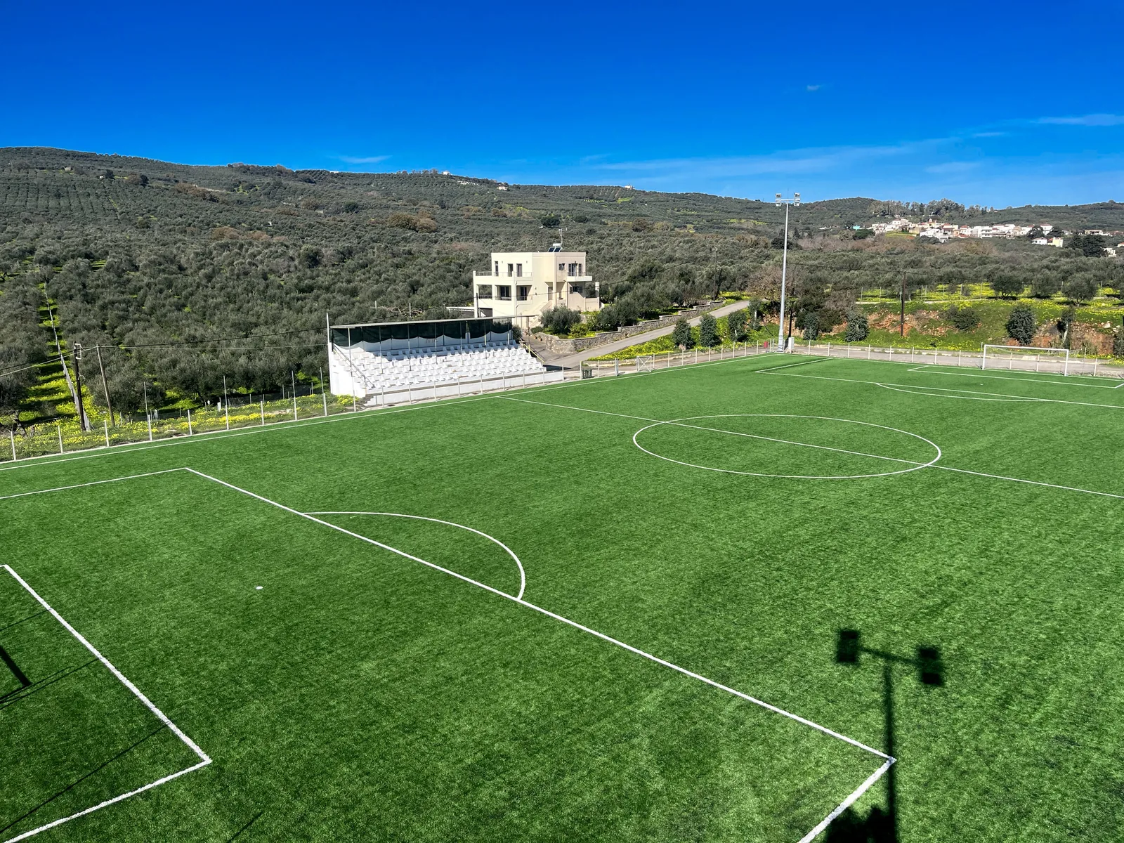 The empty grandstand and synthetic turf pitch of the Voukolies football ground by day