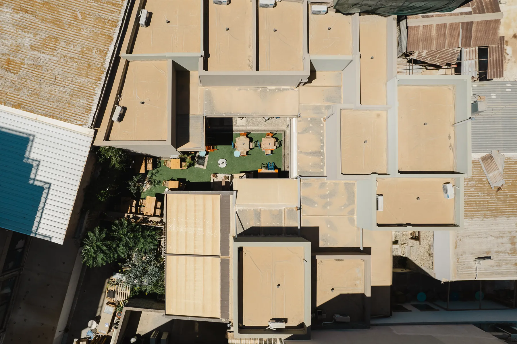 Top-down aerial of the finished market complex on Odos 1866, its roofs packed into the dense block with the planted courtyard cut into the middle