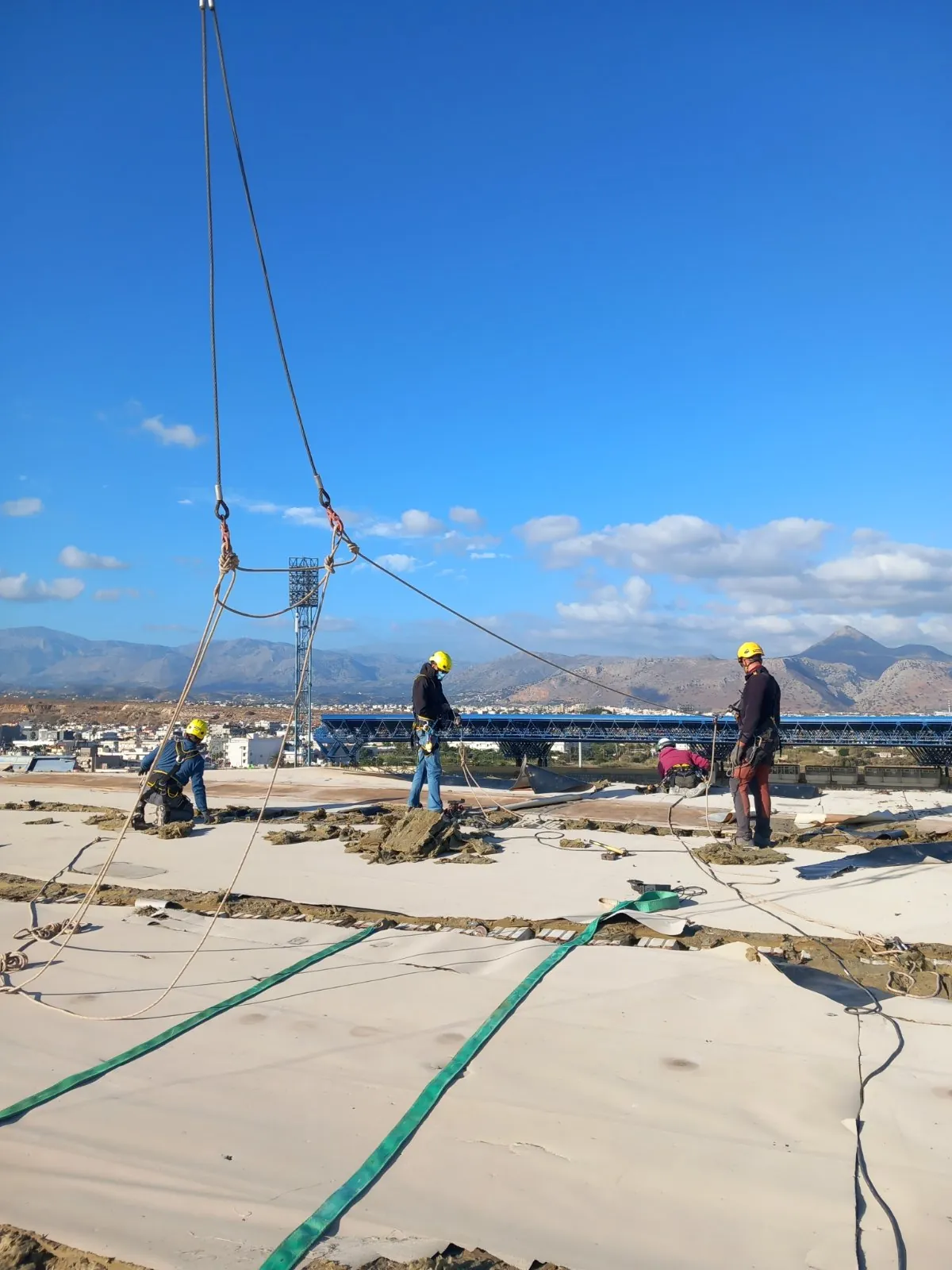 Crew working on the canopy surface at height, with the mountains behind the stadium