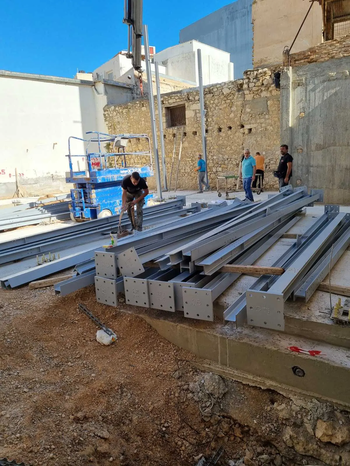 Steel sections laid out on the finished slab in May 2021, with the retained historic stone wall behind