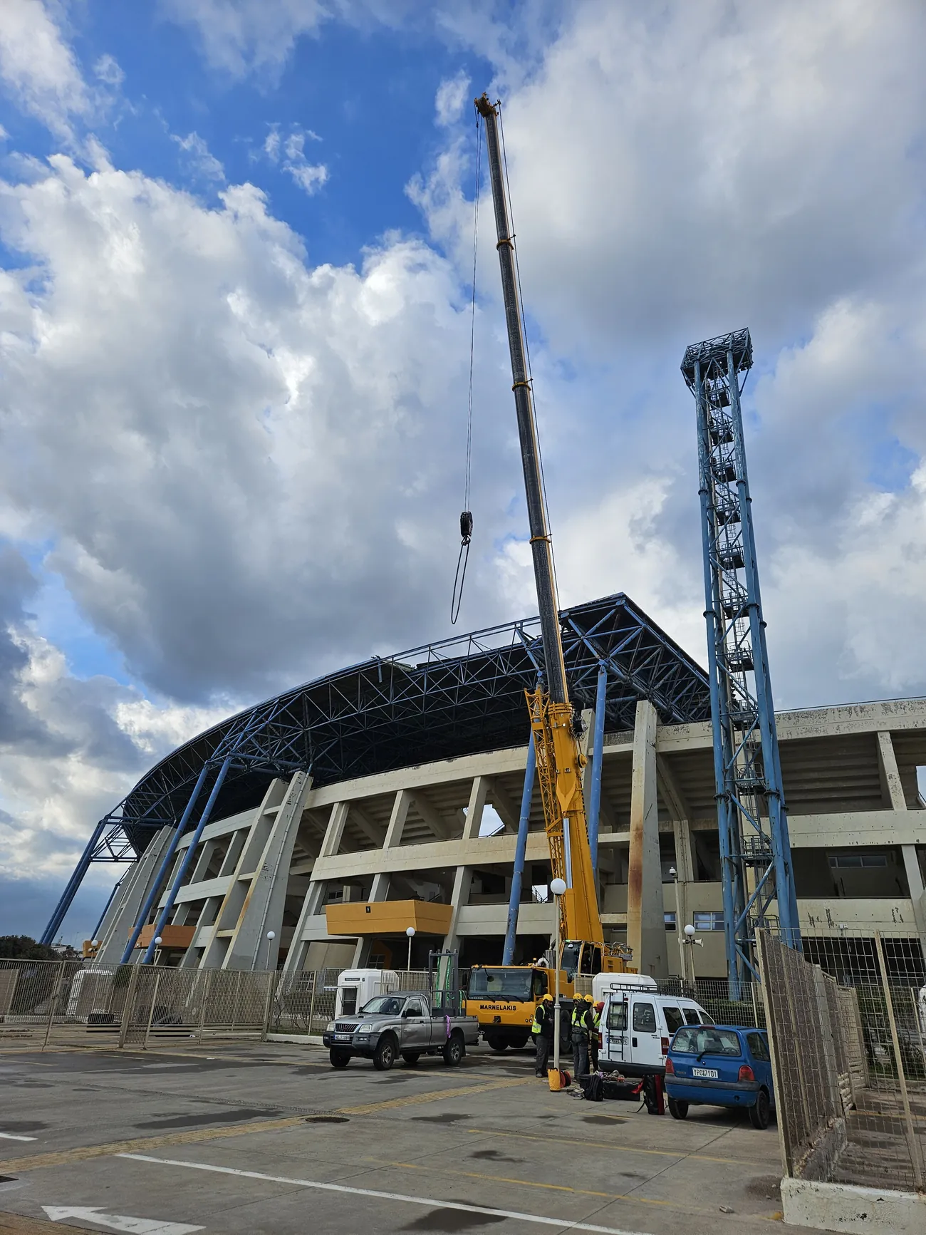 A mobile crane reaching up to the canopy alongside a floodlight mast at the stadium