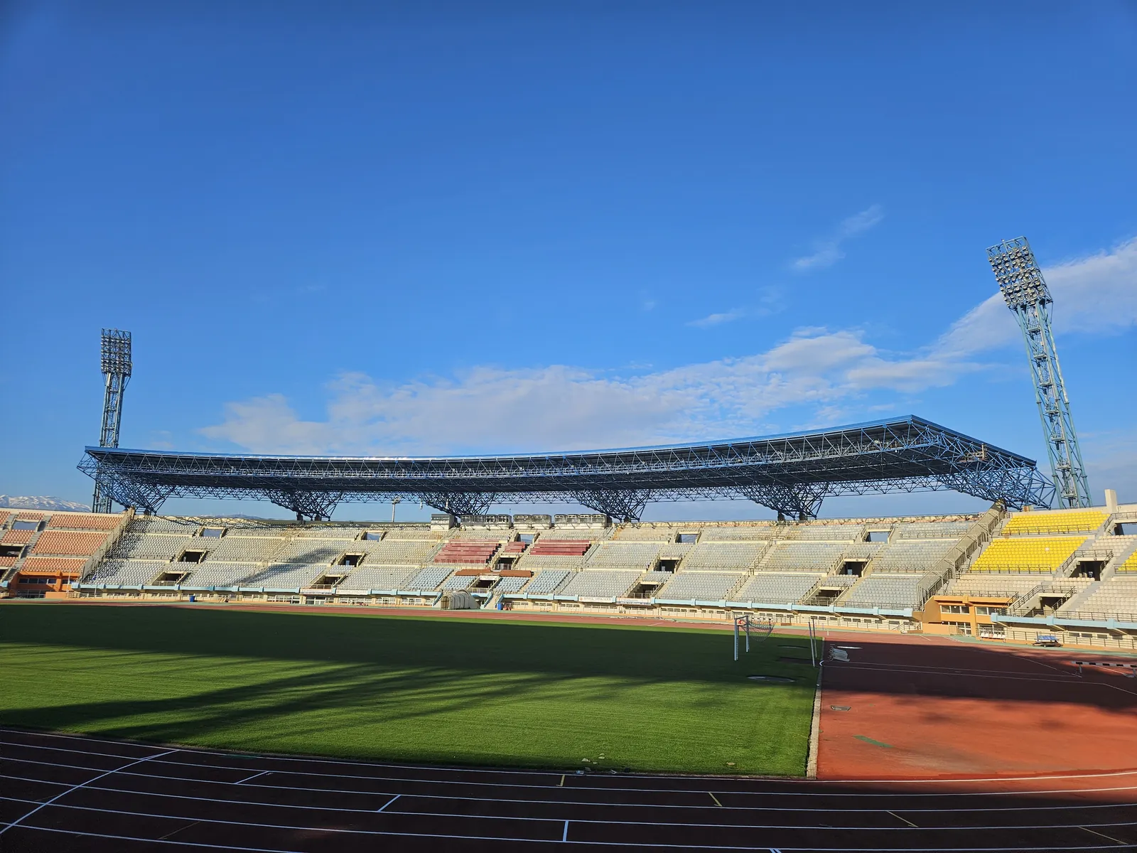 The Pancretan Stadium from inside the bowl, the west canopy spanning the main stand above empty seats, the running track and pitch