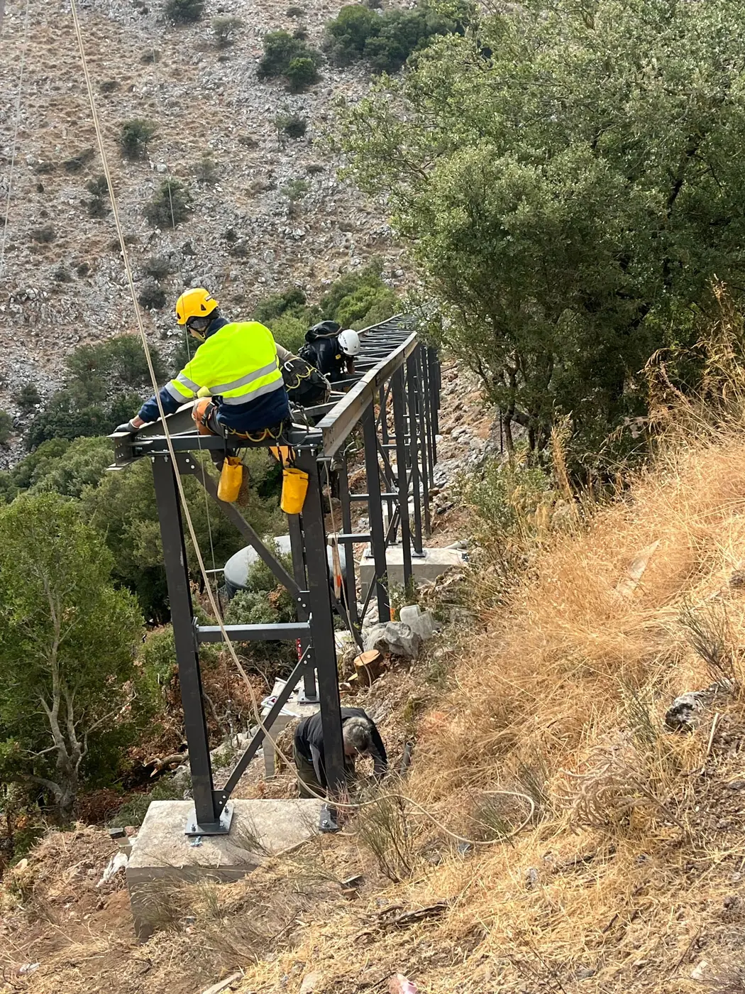 Worker in harness and helmet bolting the steel walkway structure on the steep hillside