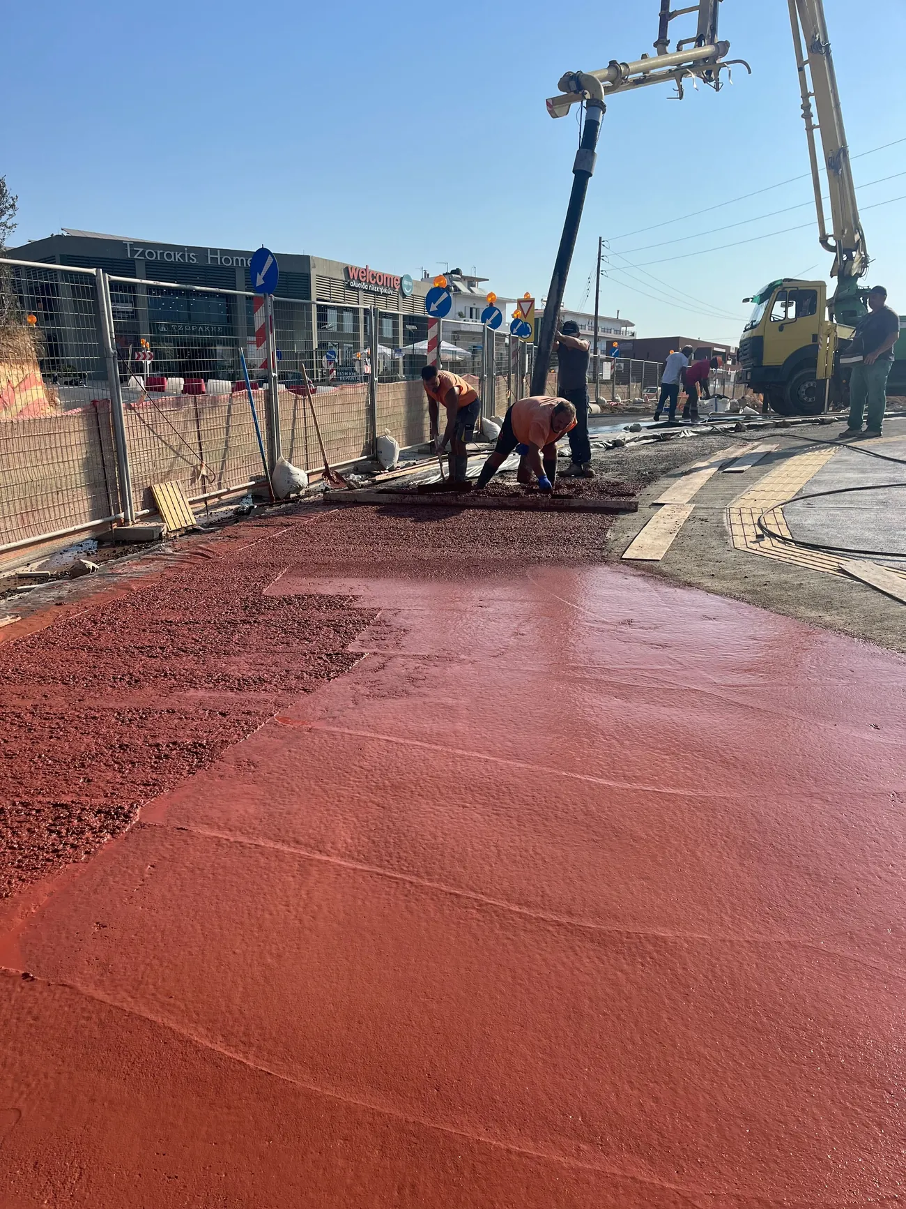 Red-pigmented concrete being placed and finished by hand for the cycle lane, with a concrete pump alongside