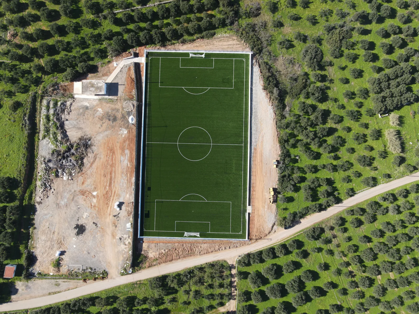 The Sisi football pitch seen from directly above — a green rectangle stamped into the olive groves