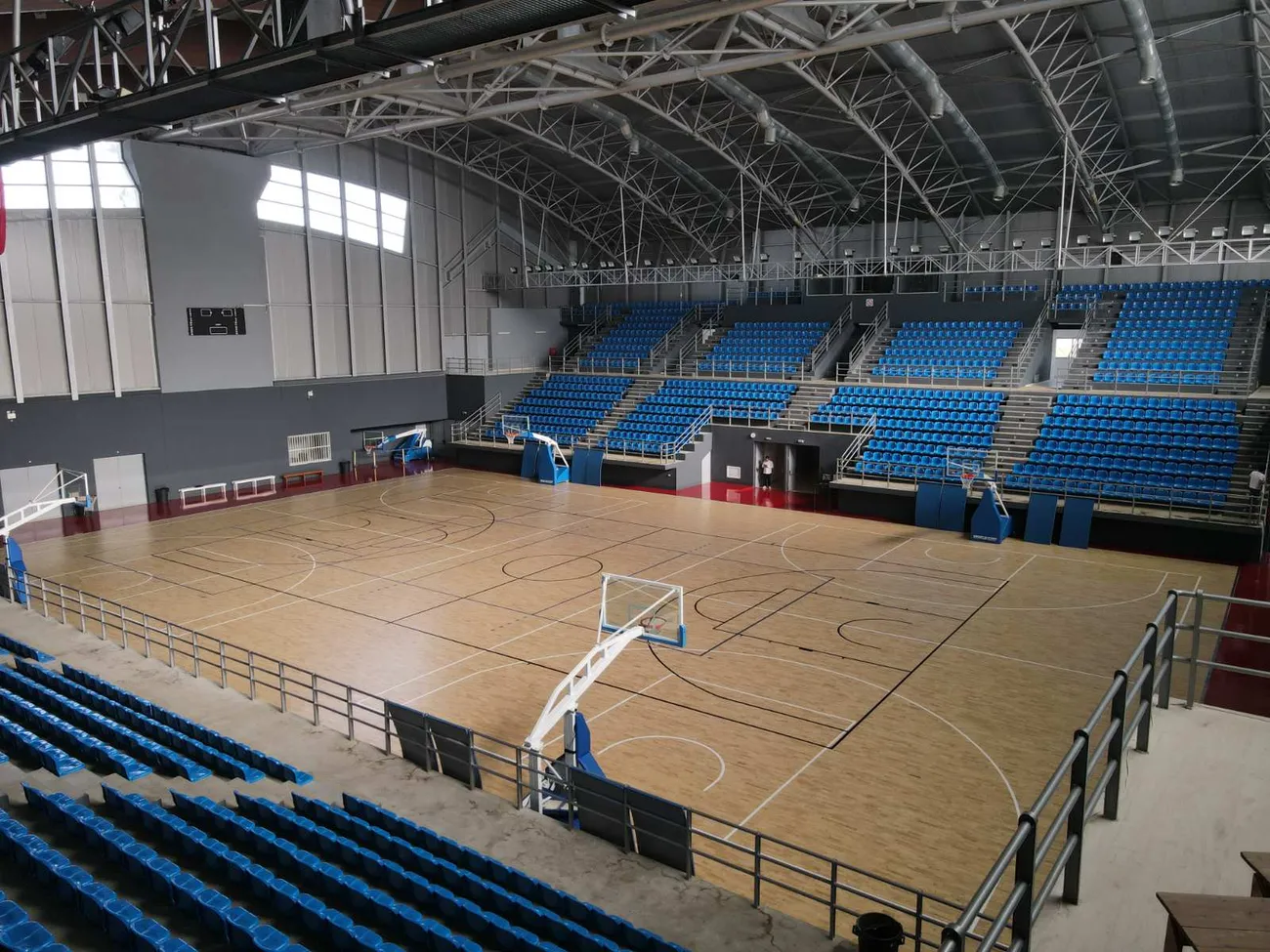 Corner view of the arena with tiered blue stands and parquet court