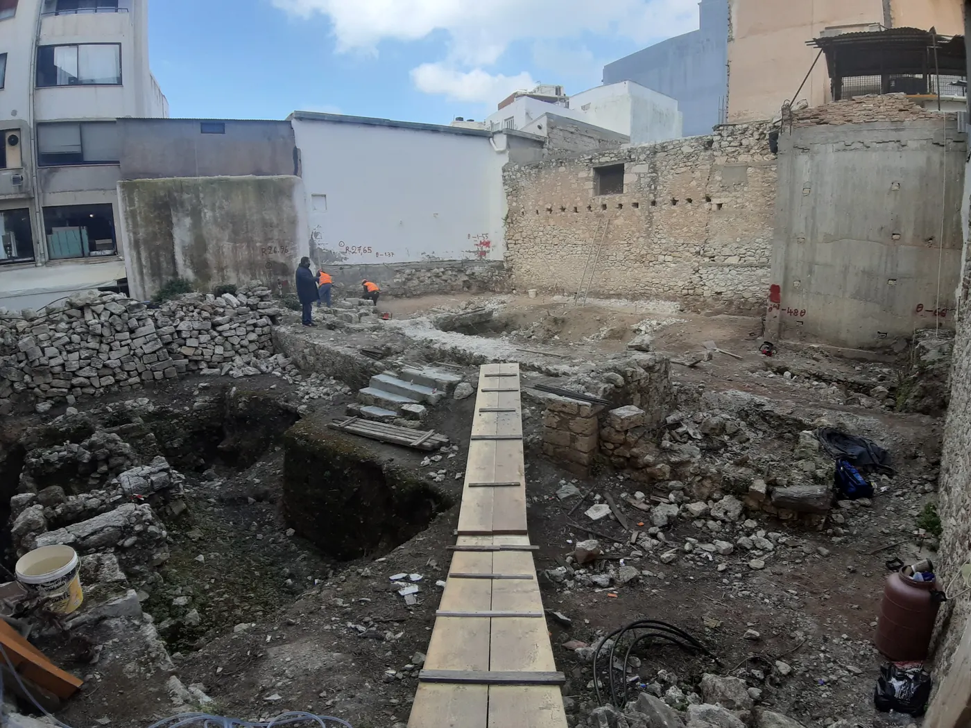 Archaeological excavation on the site in March 2021, exposed stone foundations with survey levels marked and a timber walkway laid across the dig