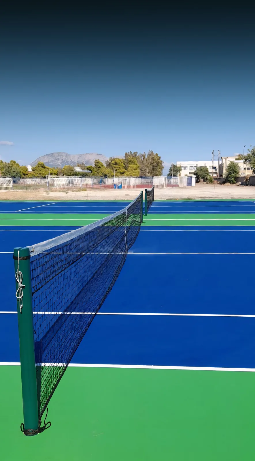 Along the net of a new blue acrylic tennis court at the Mesolongiou courts