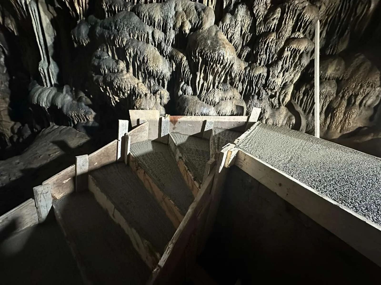 New concrete steps cast in timber formwork inside the Dikteon Cave, against a wall of stalactites