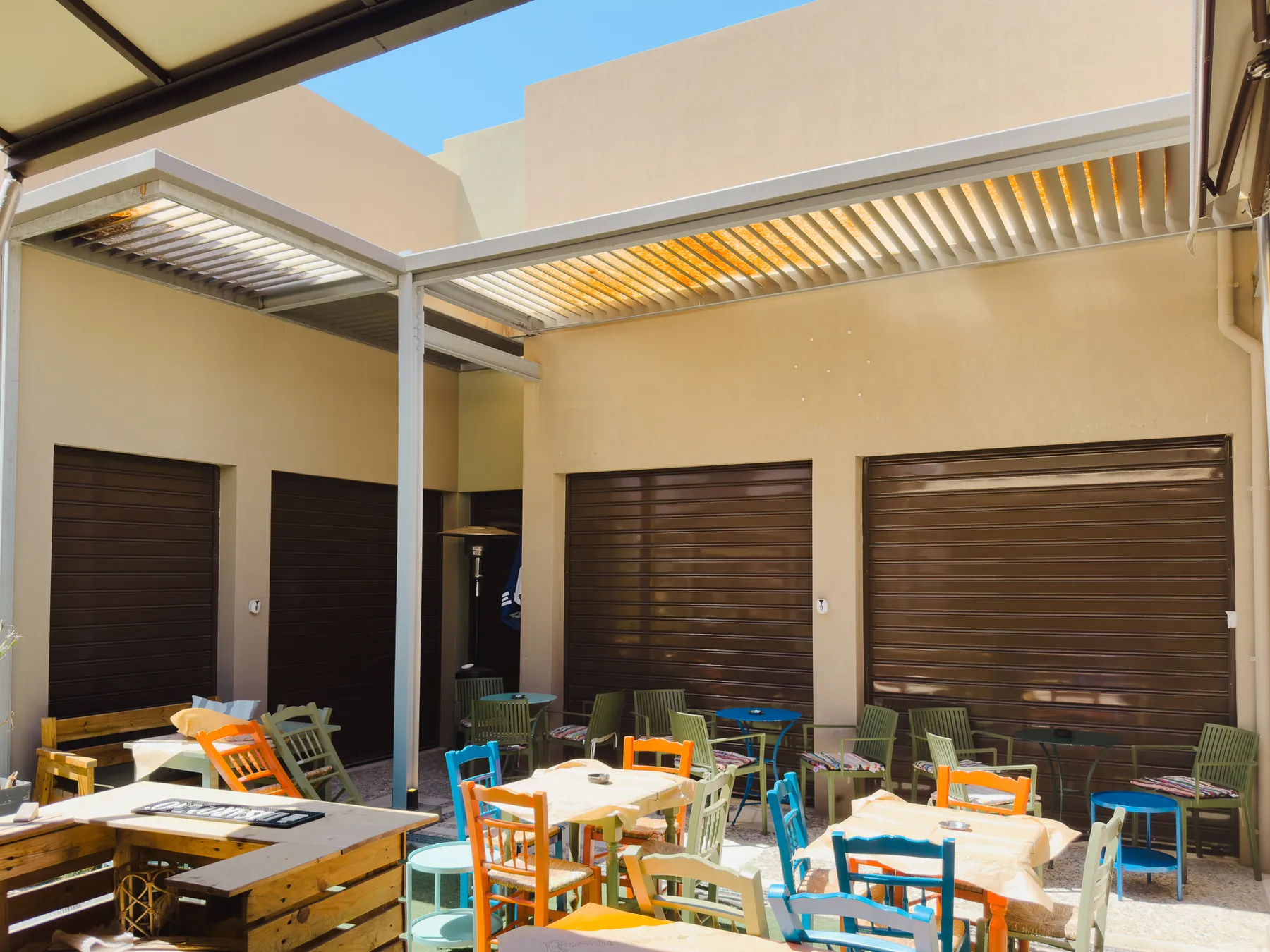 The finished courtyard with its louvred canopy, shop units behind roller shutters and painted tables and chairs set out