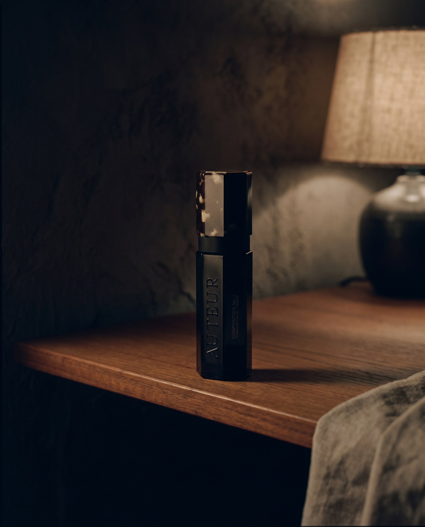 A dark glass bottle on a teak shelf under lamp light