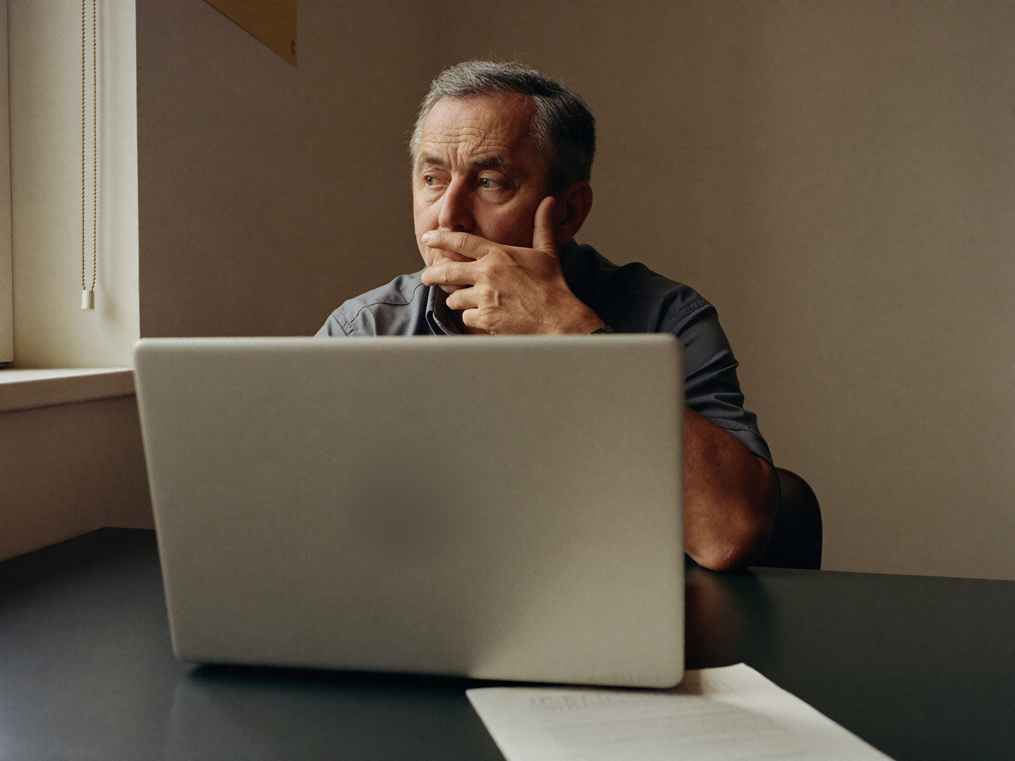 A pastor sitting at his desk, thinking, laptop open in front of him