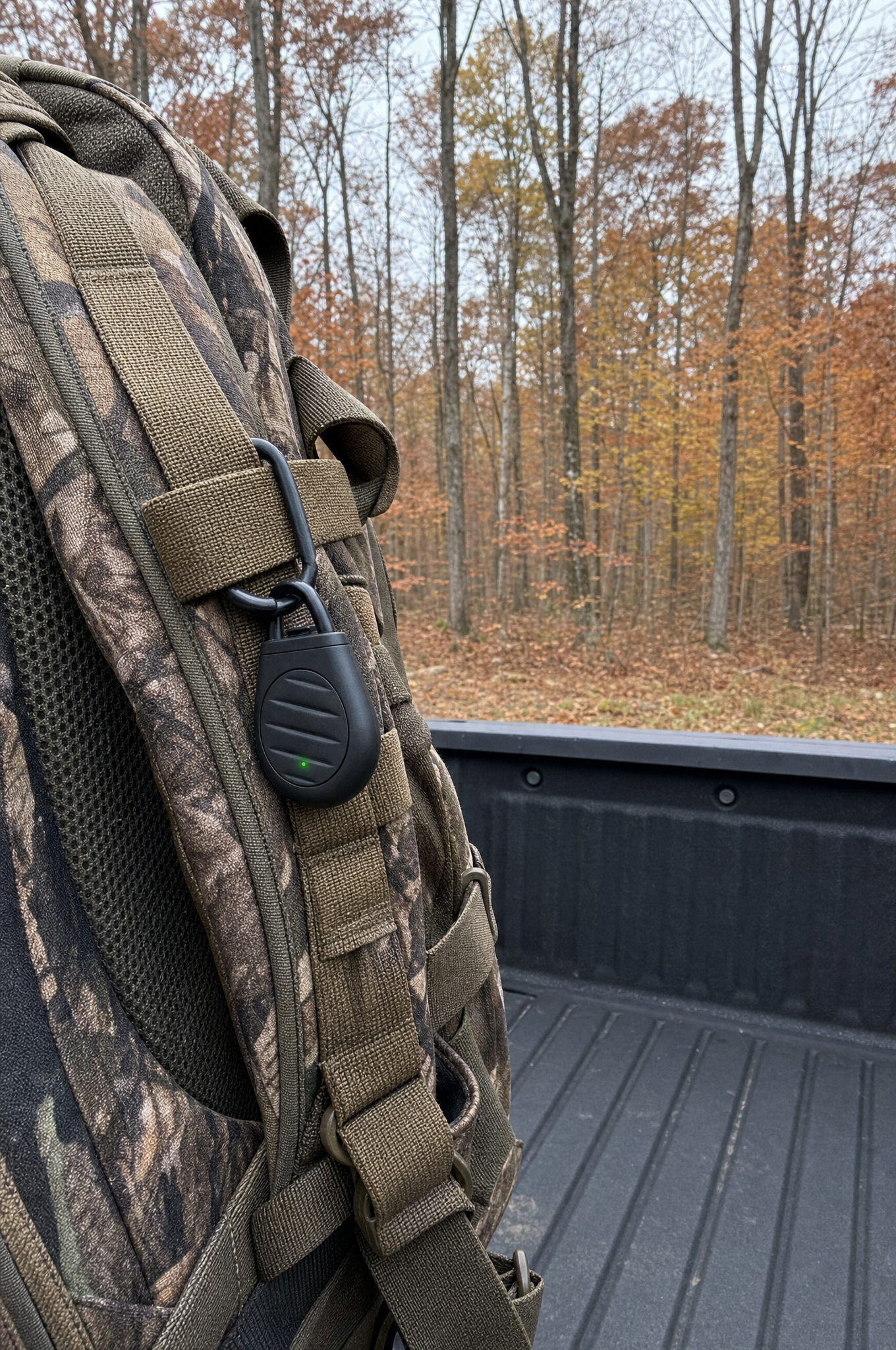 Wild Ward clipped to a camo hunting pack in the woods, green light on