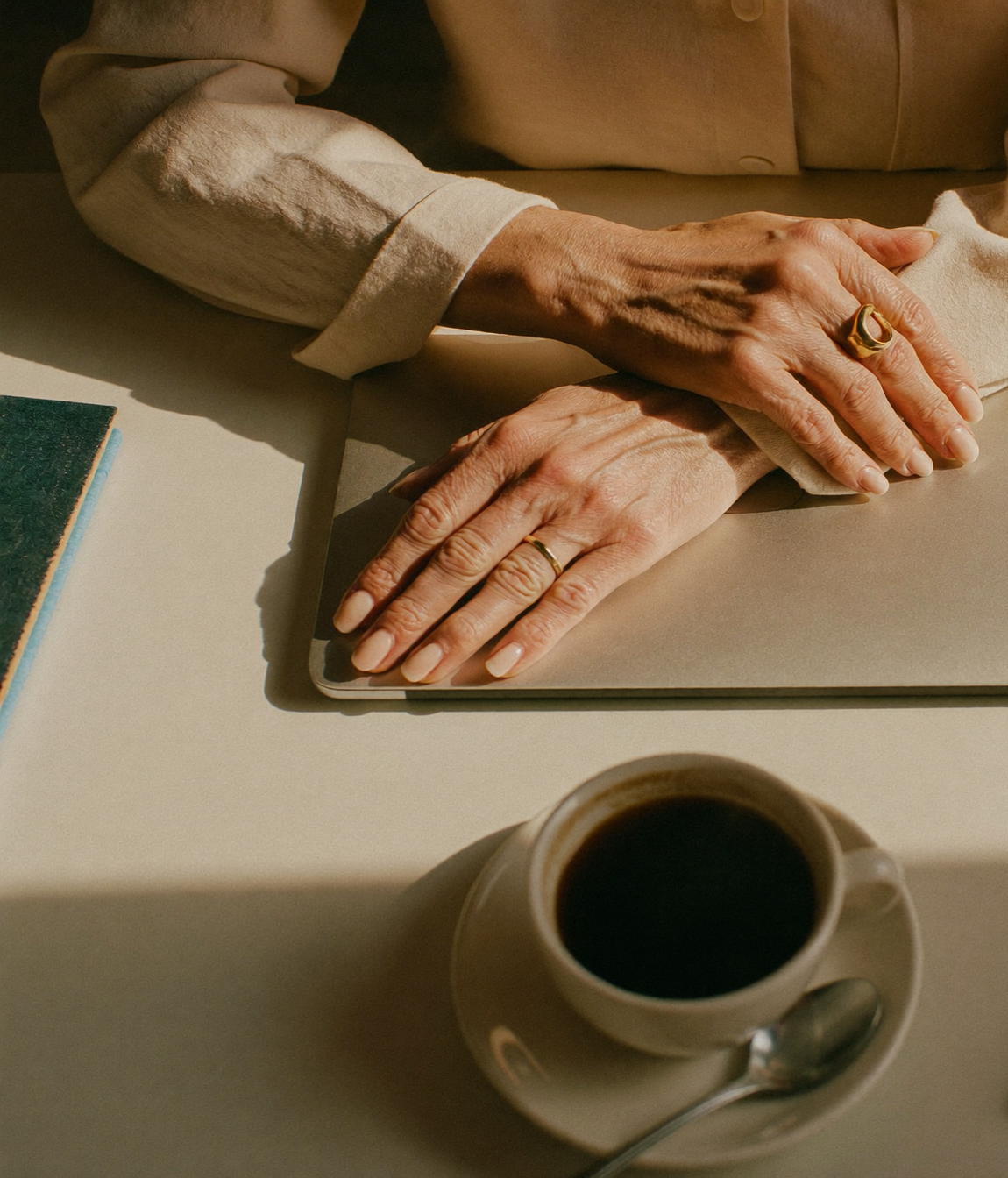 A woman's hands resting on a closed laptop beside a coffee cup