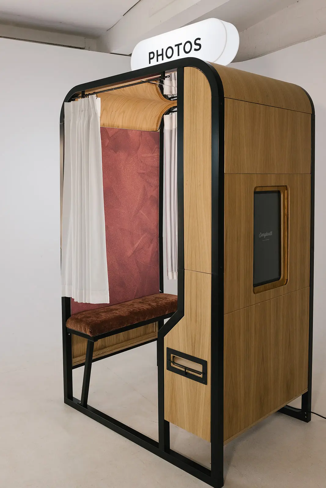 The Viva La Revival enclosed photo booth in oak and black steel, with an ivory curtain and a lit Photos sign