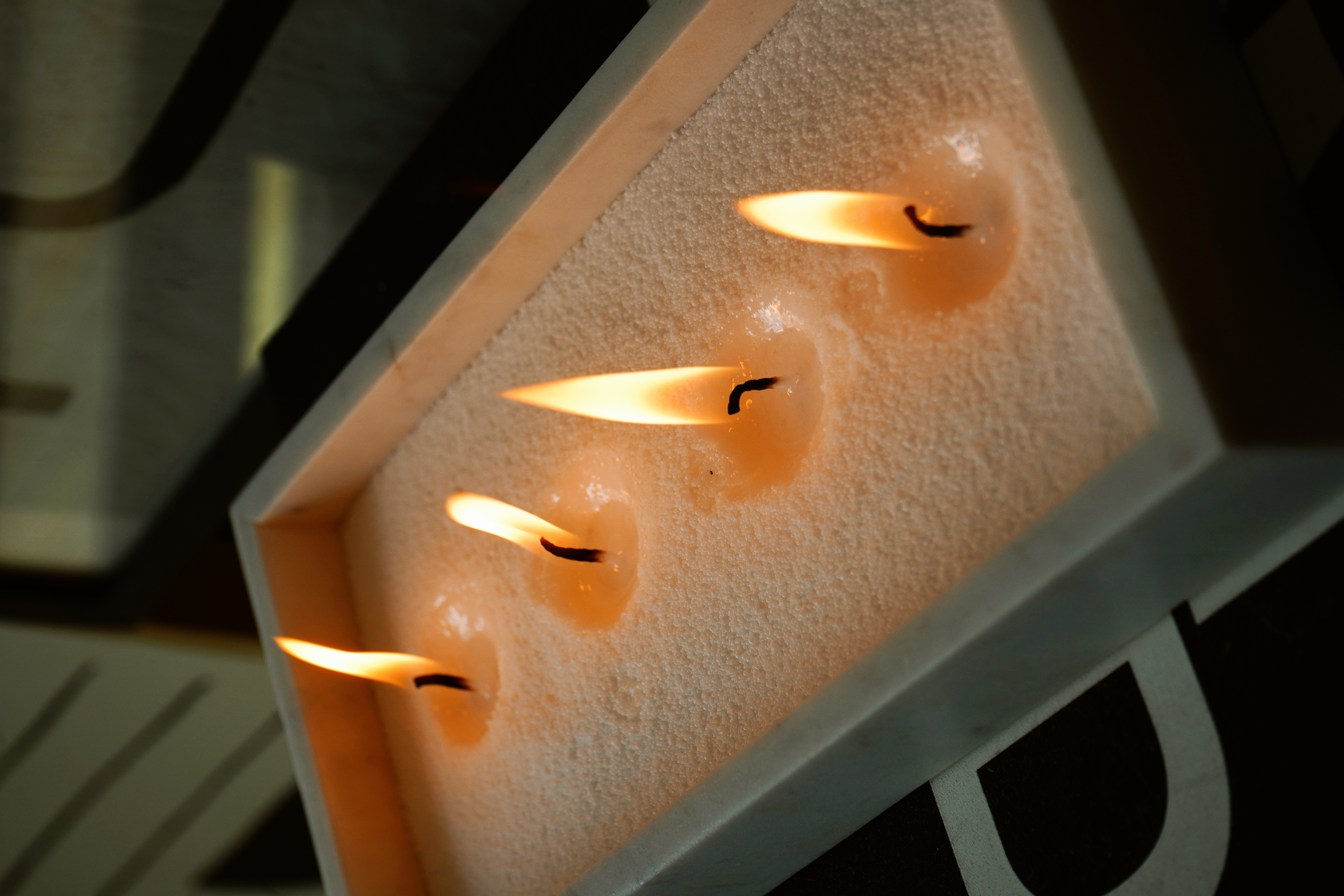 Top-down macro of a marble bowl filled with cream-white pearled candle sand, four wicks lit