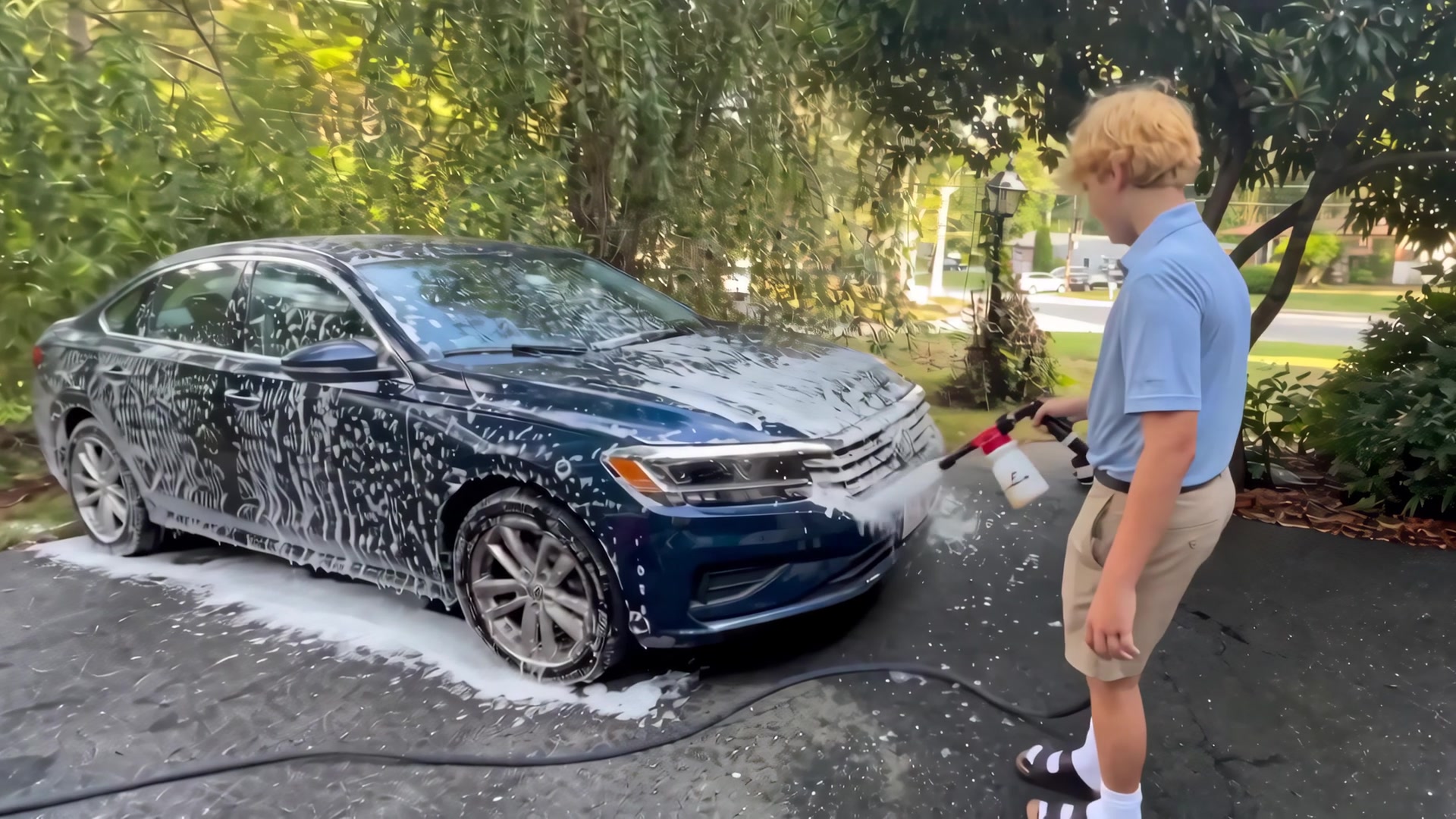 Michael spraying foam onto a sedan hood, wide shot