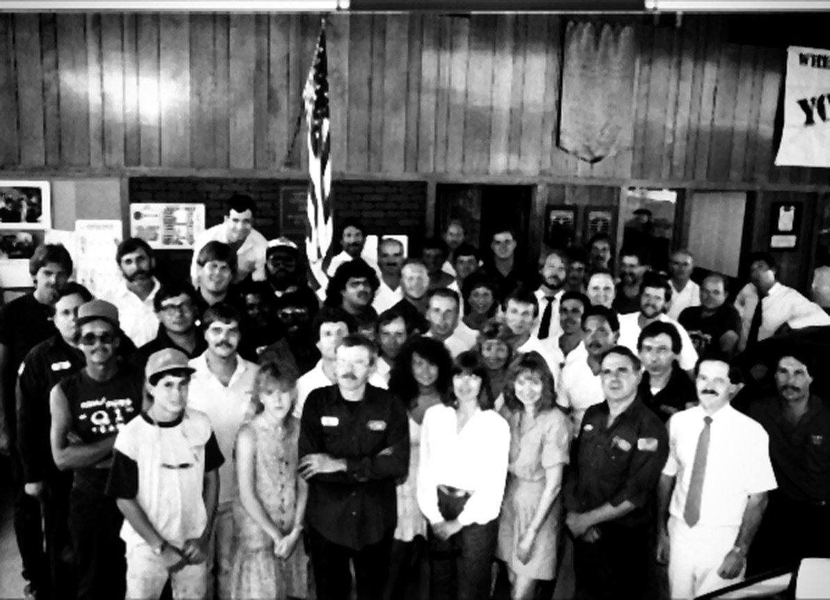 The Tom's Ford team in the 1980s, gathered in the old showroom under the flag