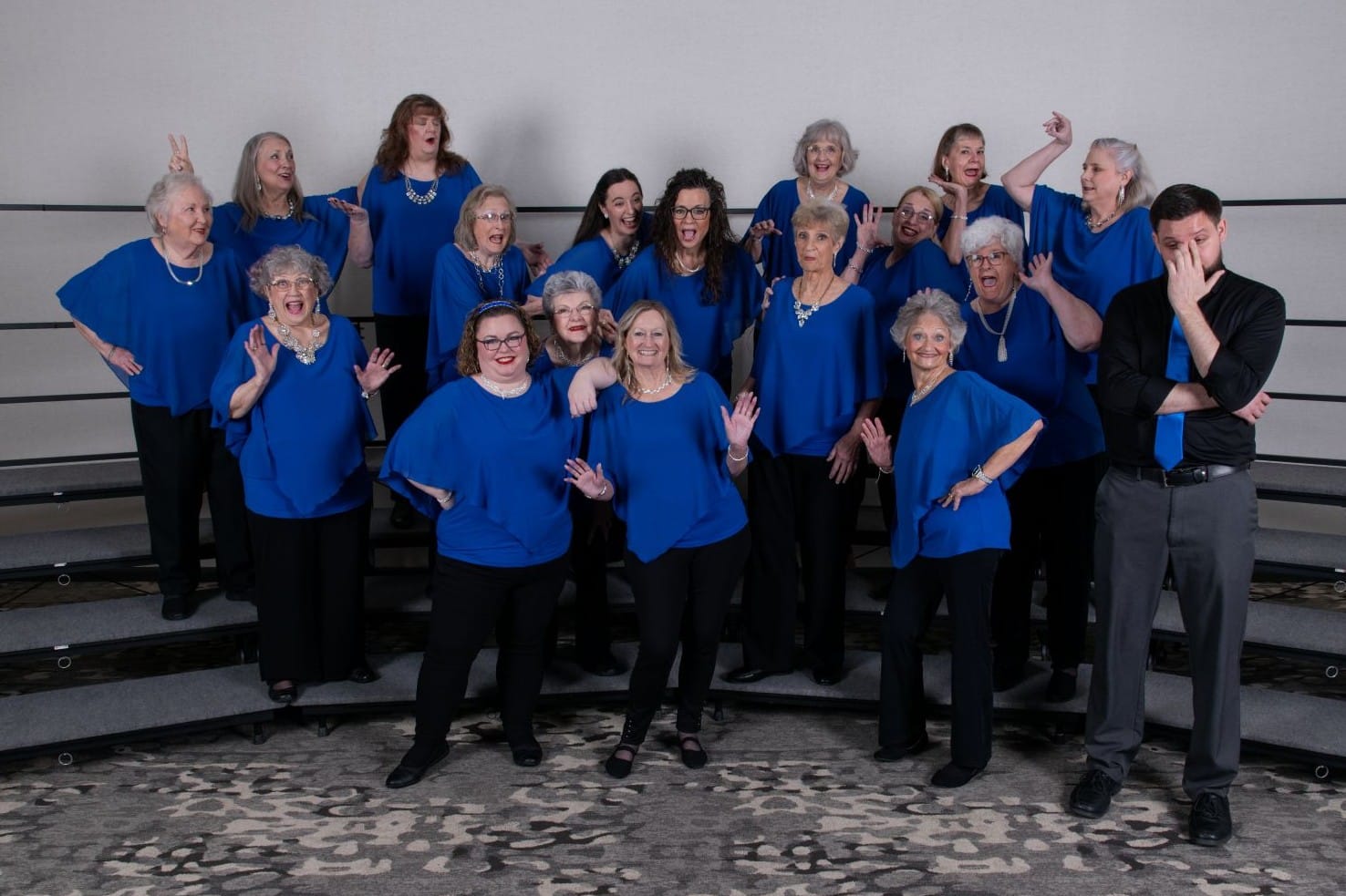 The chorus in blue tops laughing with their arms in the air after a performance