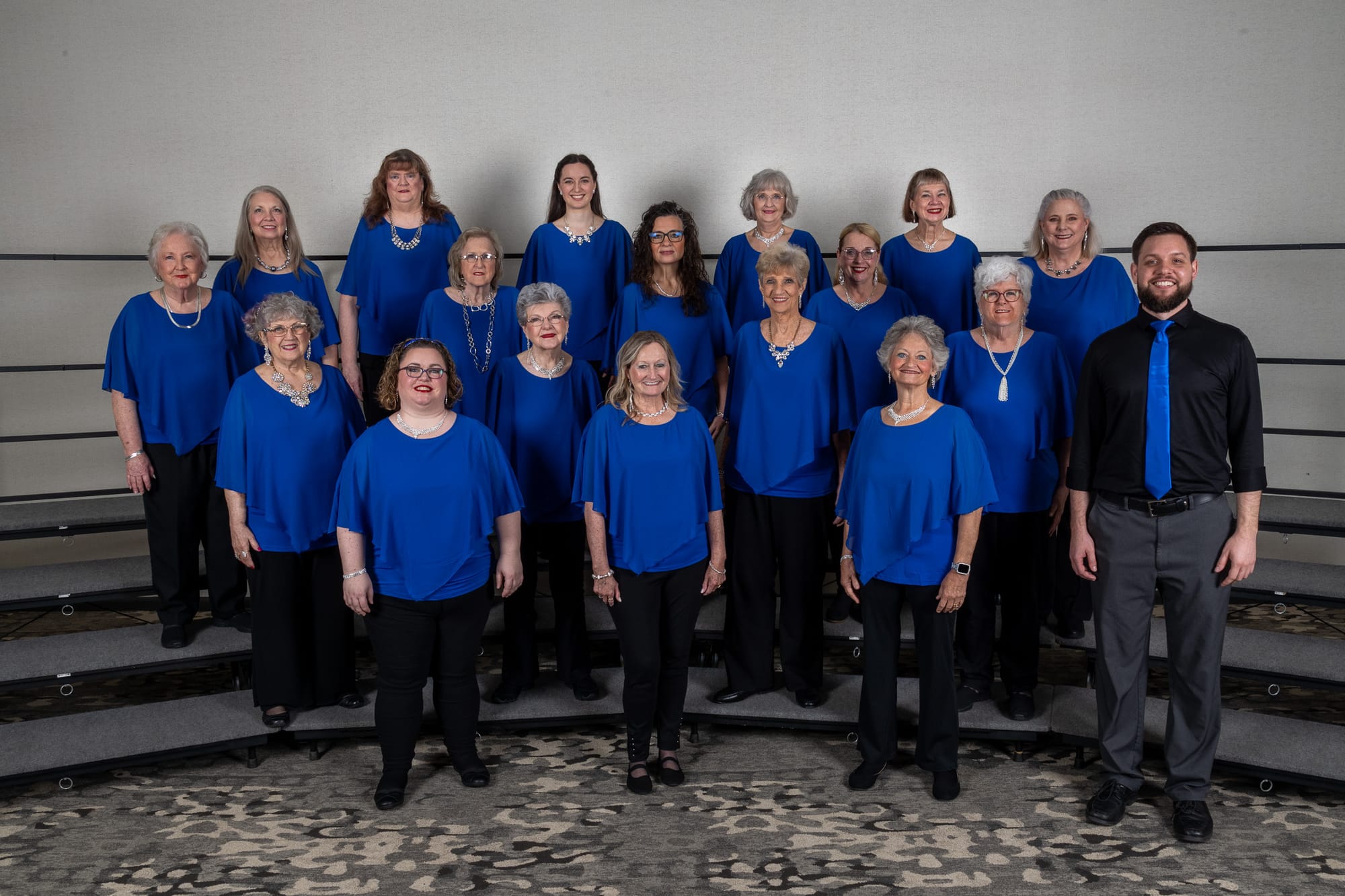 The full White Sands A Cappella chorus on risers, in matching blue tops, with their director