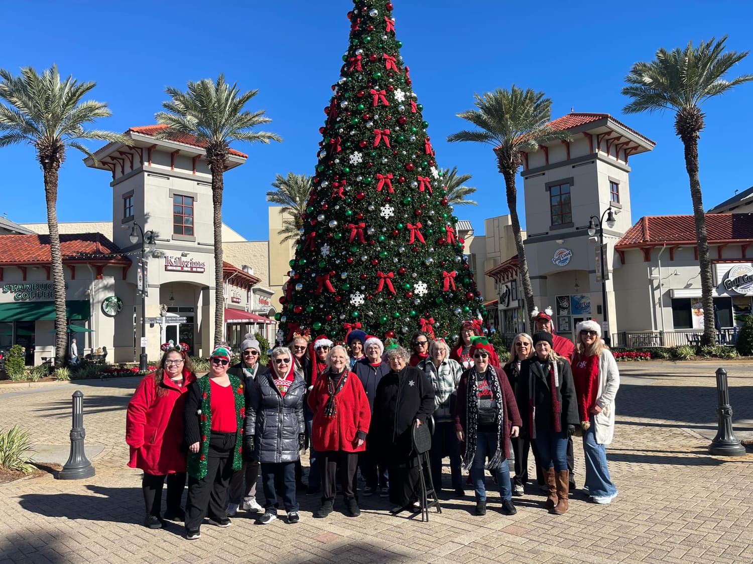 The chorus gathered outdoors by a large Christmas tree at Destin Commons