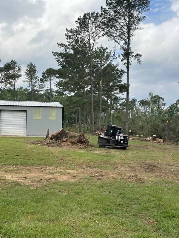 The grinder working beside a shop building with a pile of cut brush and limbs alongside