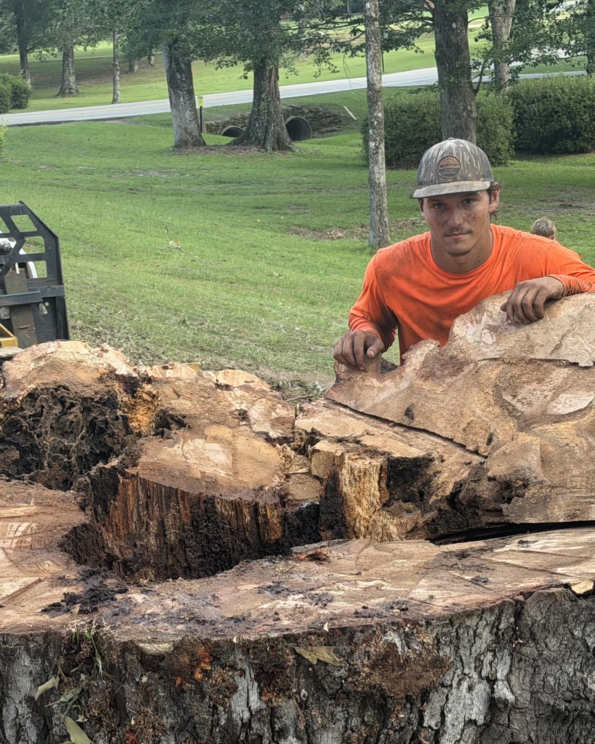 Chris of Burton Stump Removal standing behind the cut face of a huge tree trunk on a job site, with his equipment behind him