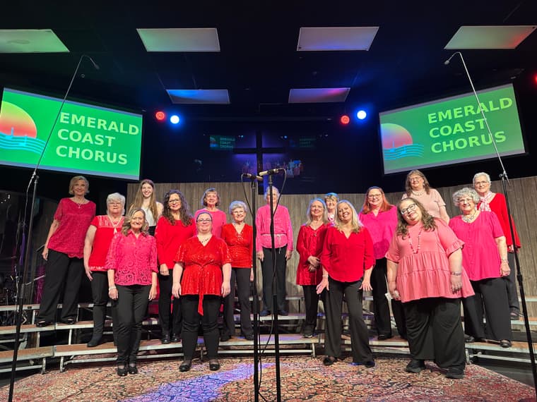 The chorus in red on a dark stage at the Emerald Coast Chorus show