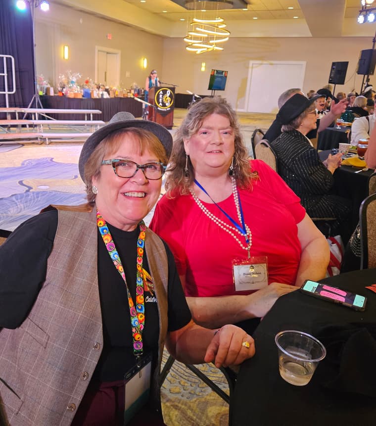 Two members in hats and beads at the convention dinner