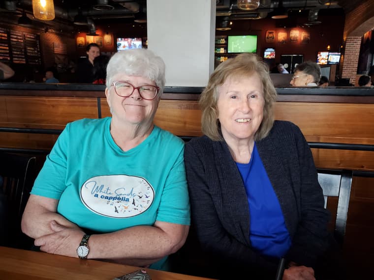 Two chorus members smiling in a restaurant booth
