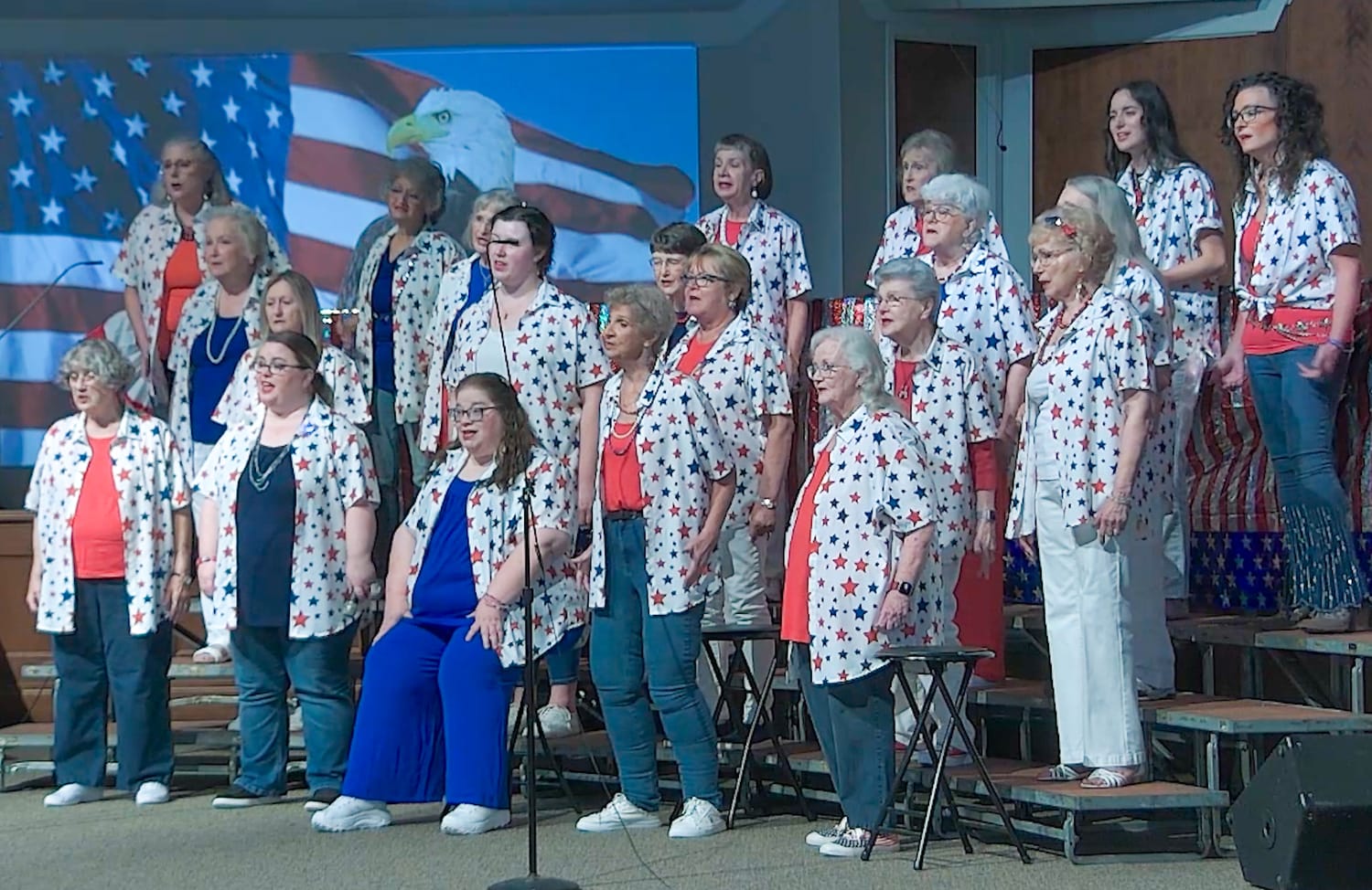 The chorus singing on stage in front of a stars and stripes backdrop