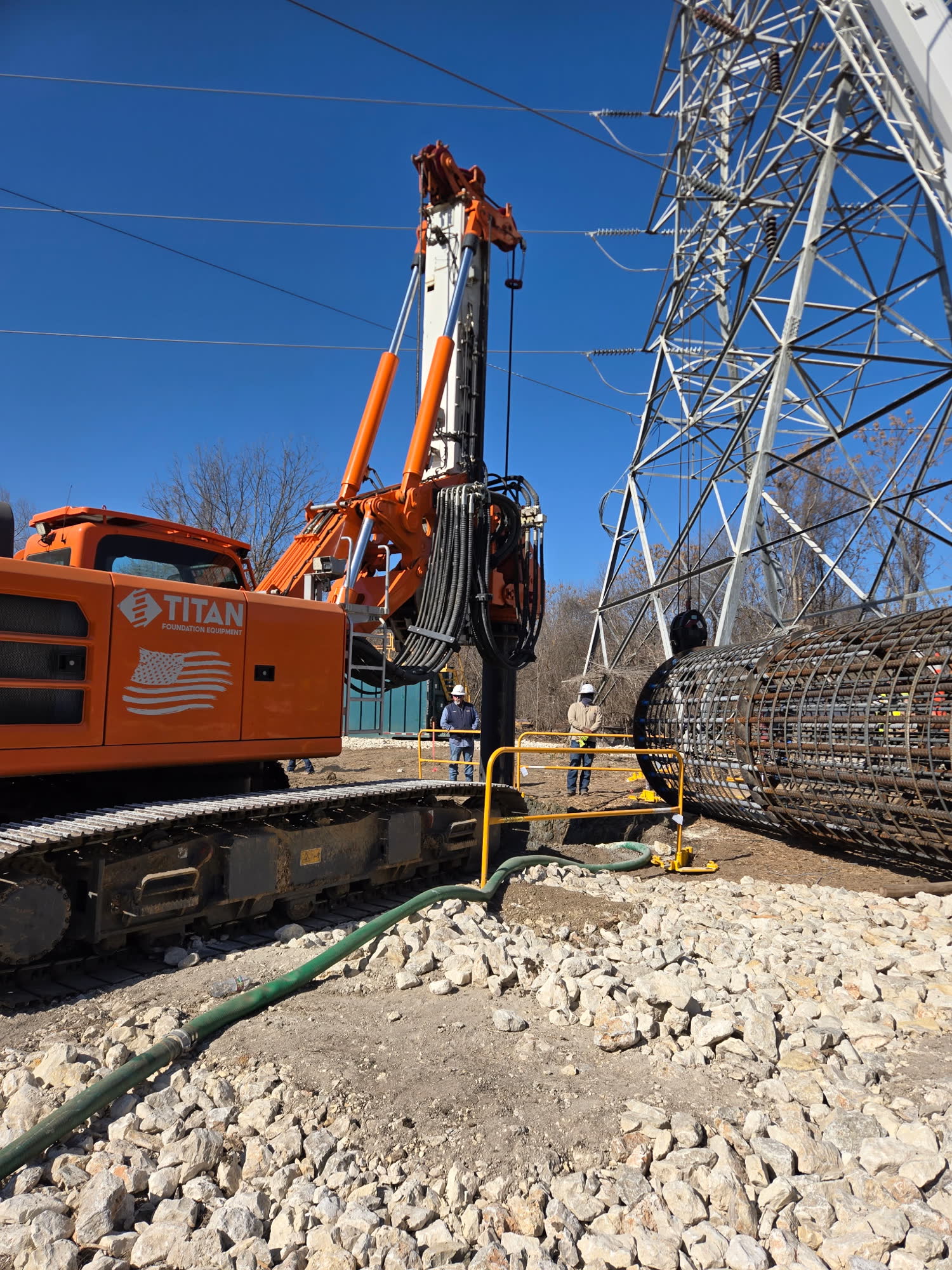 C & M Foundations drill rig setting a rebar cage beside a transmission tower
