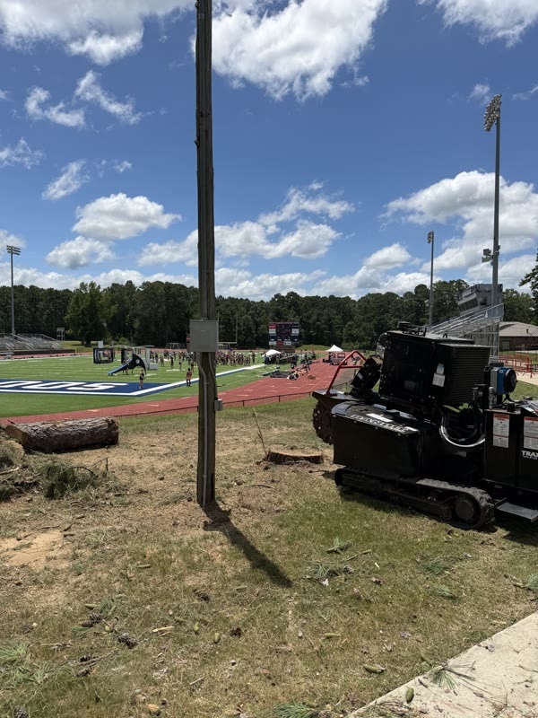 Burton Stump Removal grinder working a stump out along the fence line beside a school track and football field