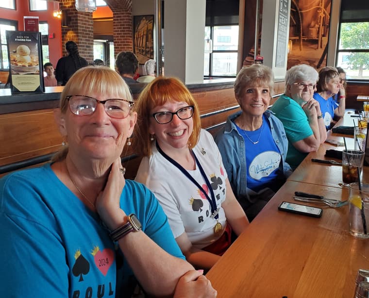 Chorus members smiling together around a restaurant table