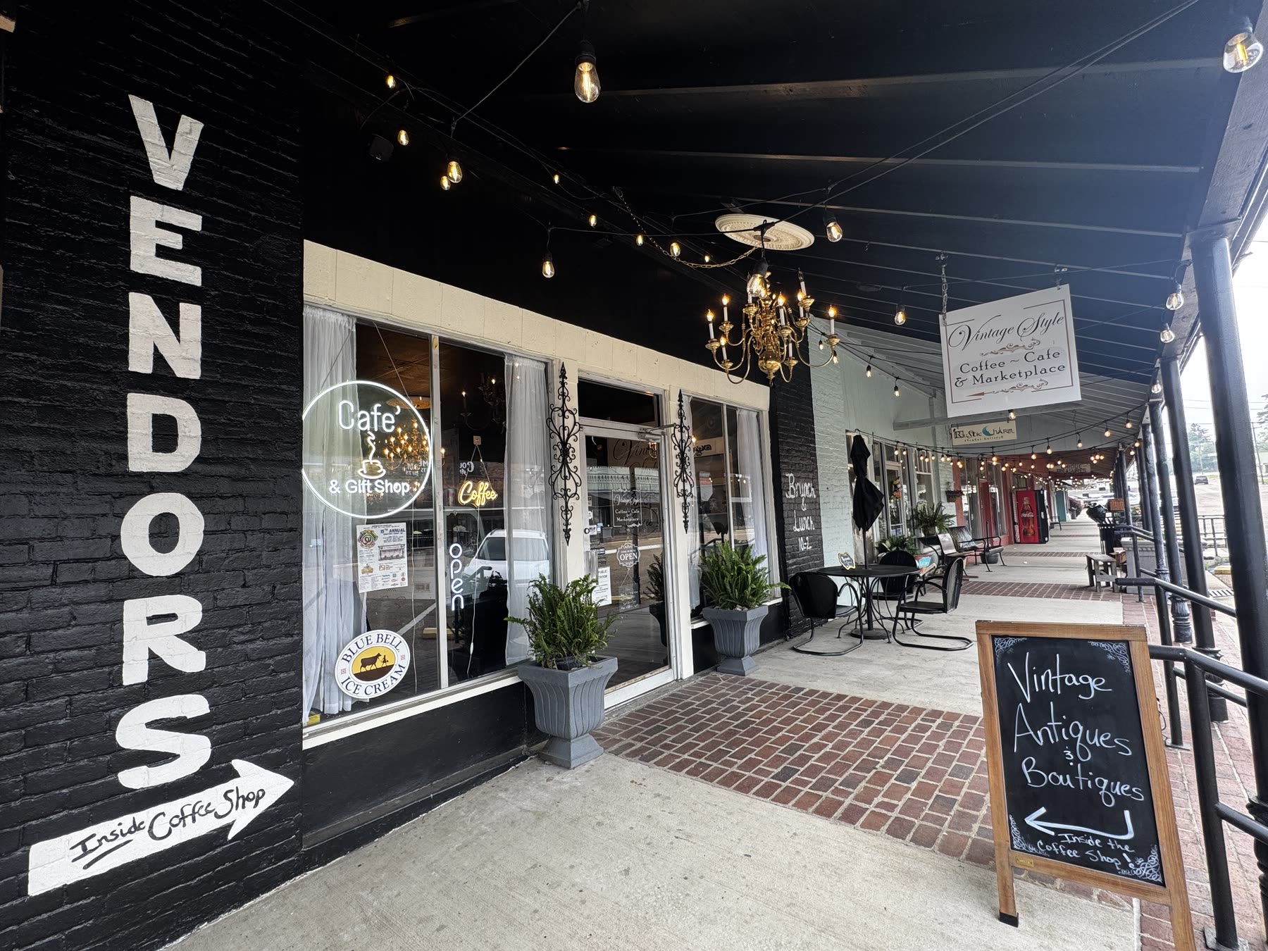The Vintage Style storefront on the corner in downtown Summit, with VENDORS painted down the black brick and cafe tables under the awning