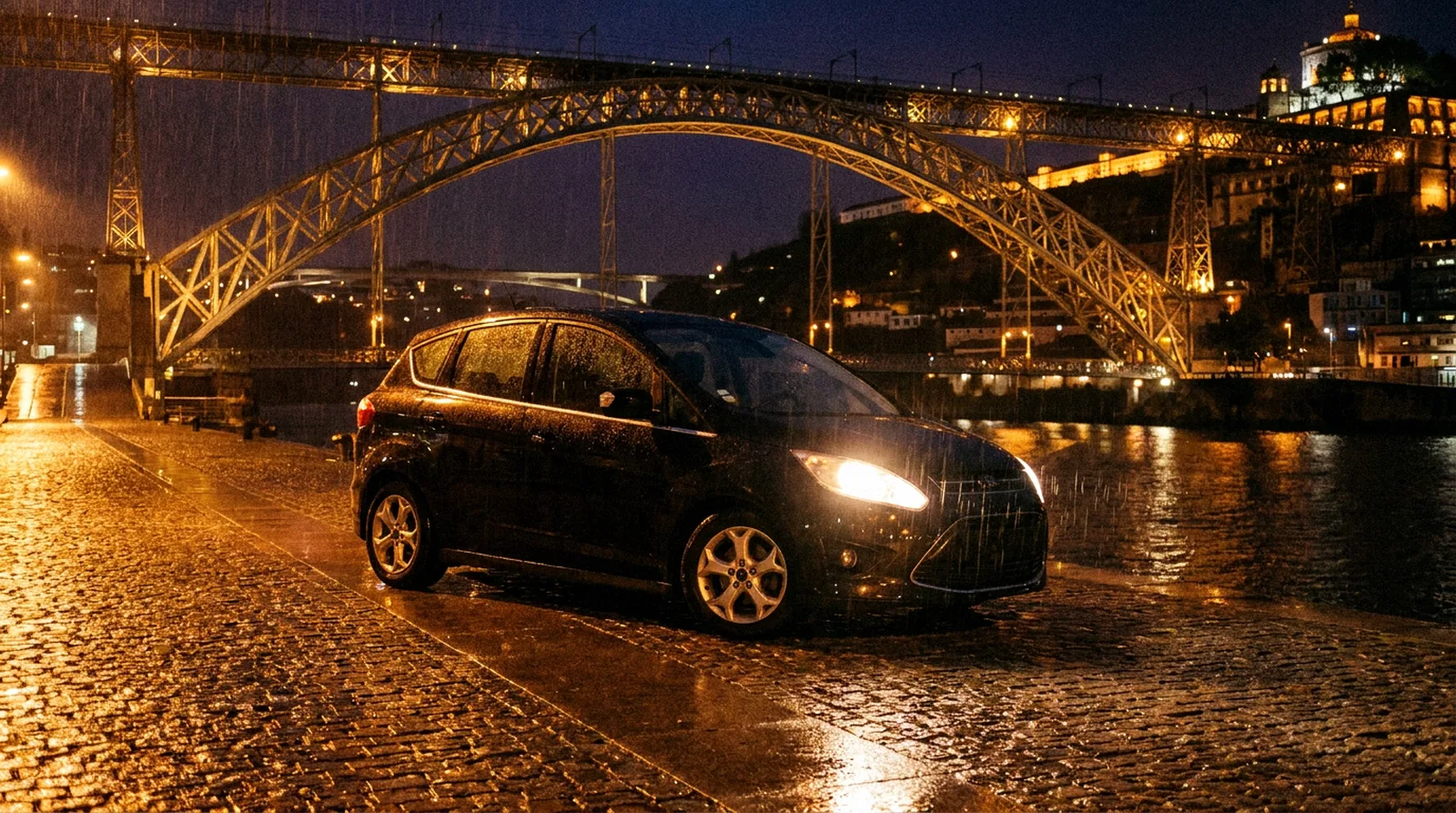 Zwarte auto op natte klinkers aan het water, met een verlichte boogbrug op de achtergrond